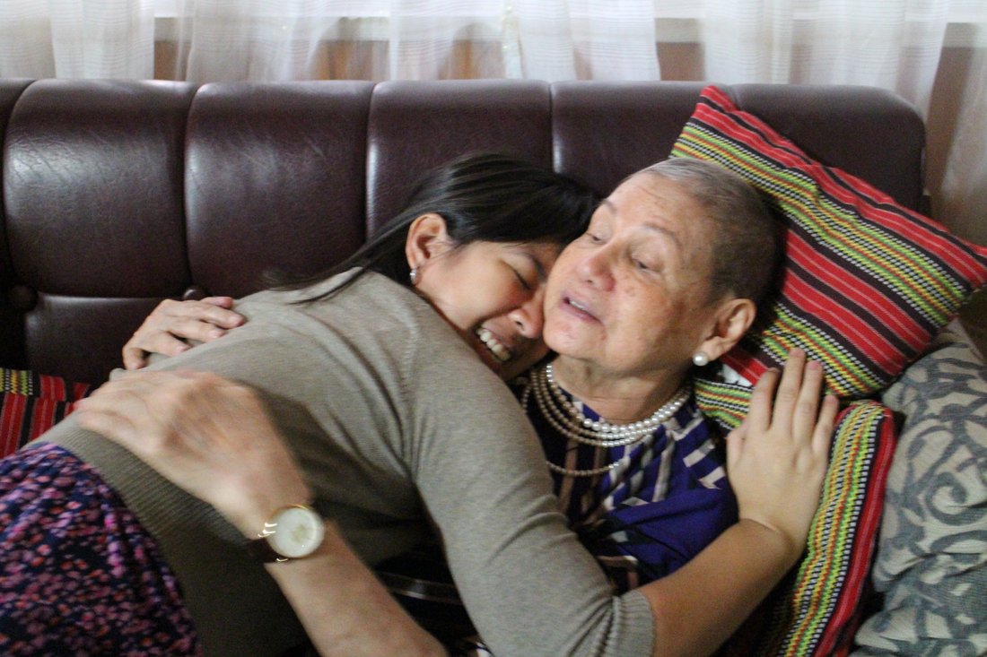 Paulina embracing her grandmother tightly on a couch, cheek to cheek, both emotional.