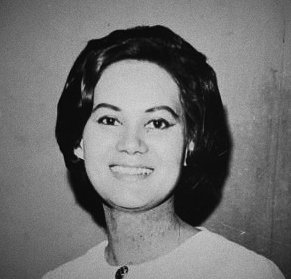 A black-and-white studio portrait of a young woman, smiling, from the 1960s.