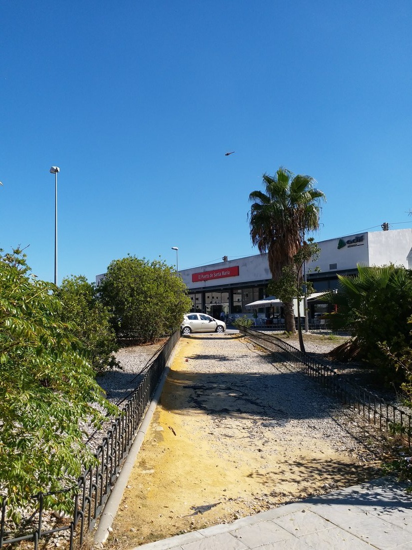 A gravel path under a bright blue sky leading toward a building reading El Puerto de Santa María.