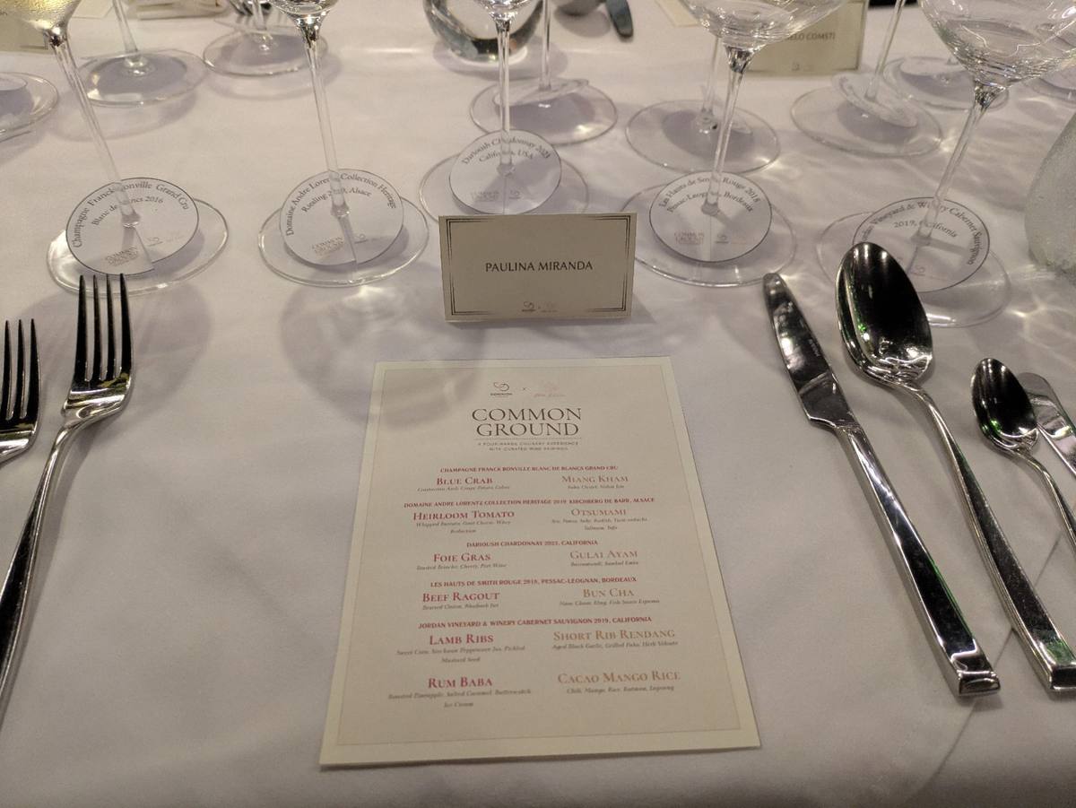 A set table at Common Ground: five wine glasses, silverware, a place card reading Paulina Miranda, and the printed menu.