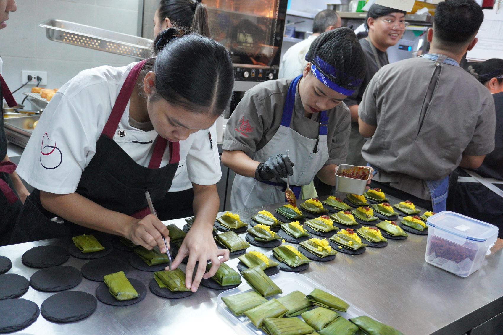 The kitchen line plating banana-leaf parcels with turmeric rice and chilli.